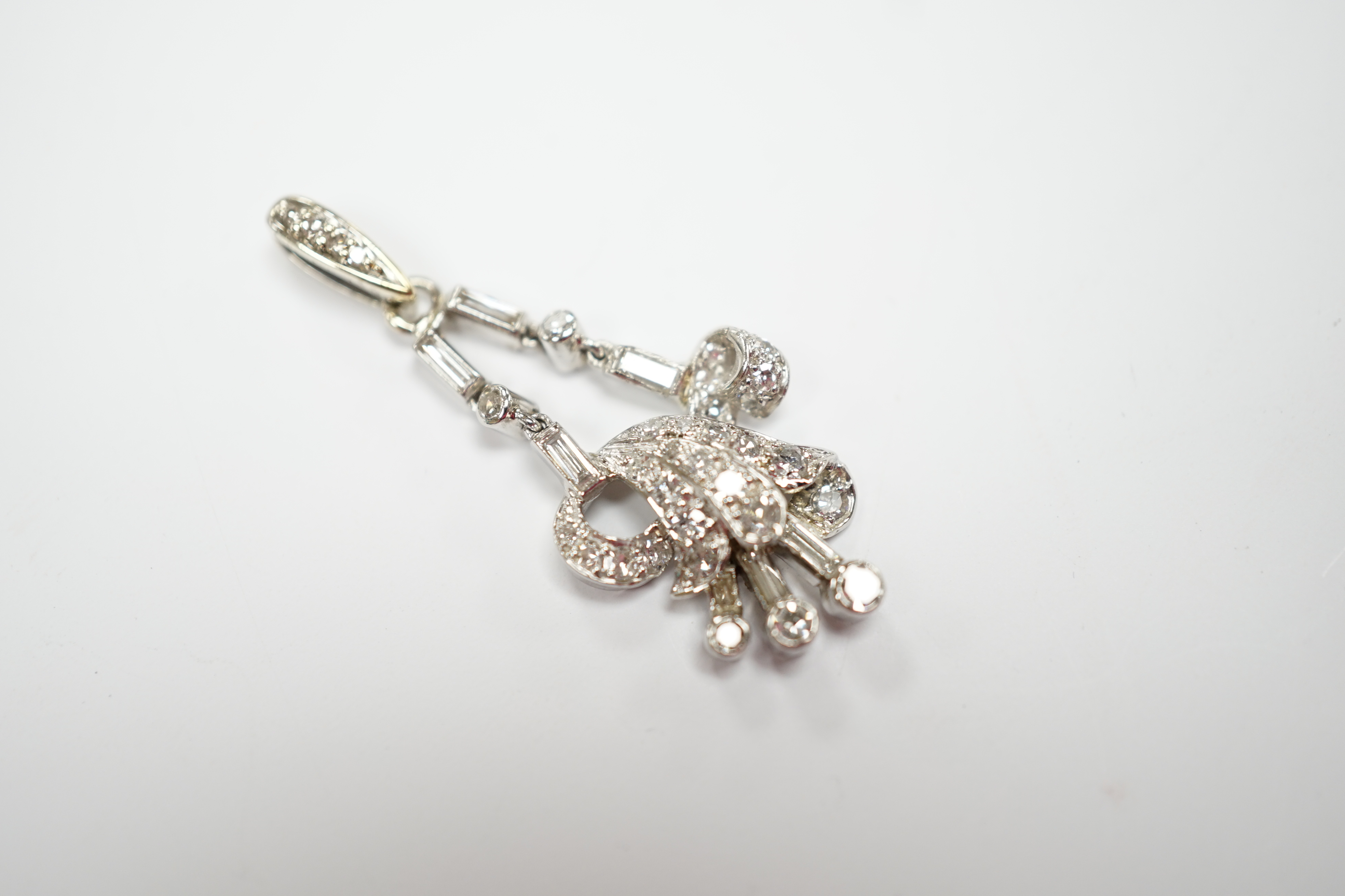 A white metal baguette and round cut diamond cluster set scroll pendant, overall 33mm, gross weight 3.6 grams.